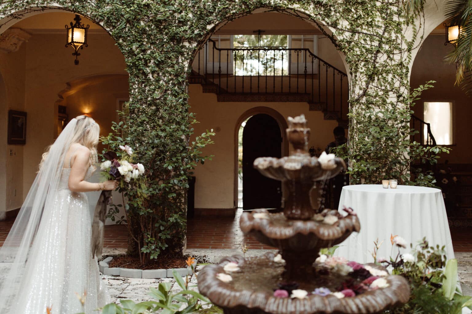 ride admiring floral arrangements by a miami wedding florist at a courtyard fountain at villa woodbine