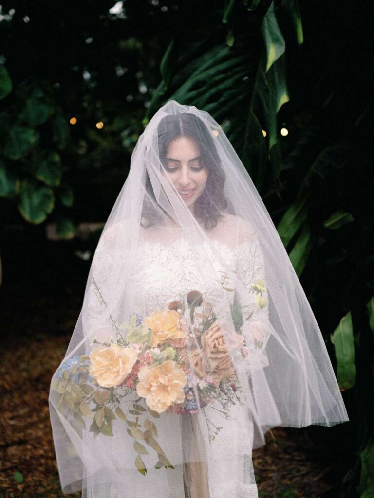 smiling bride under a veil holding a bouquet, with Miami Beach garden wedding florals