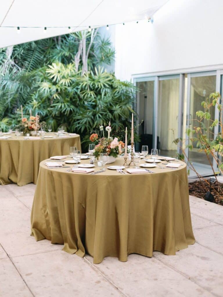 golden hour wedding dinner setup with sand-colored taper candles and floral centerpiece in miami beach botanical garden.