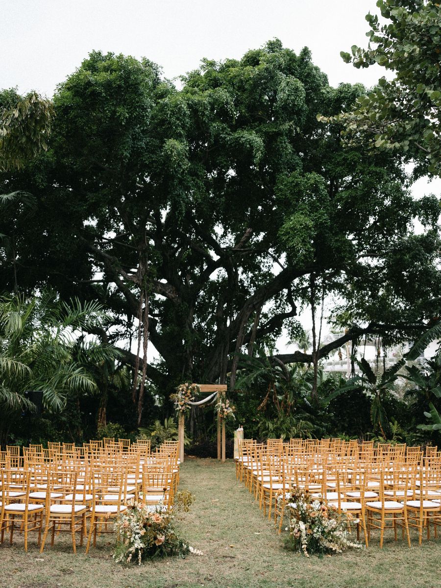 outdoor wedding ceremony setup with wooden chairs and floral chuppah at miami beach garden.