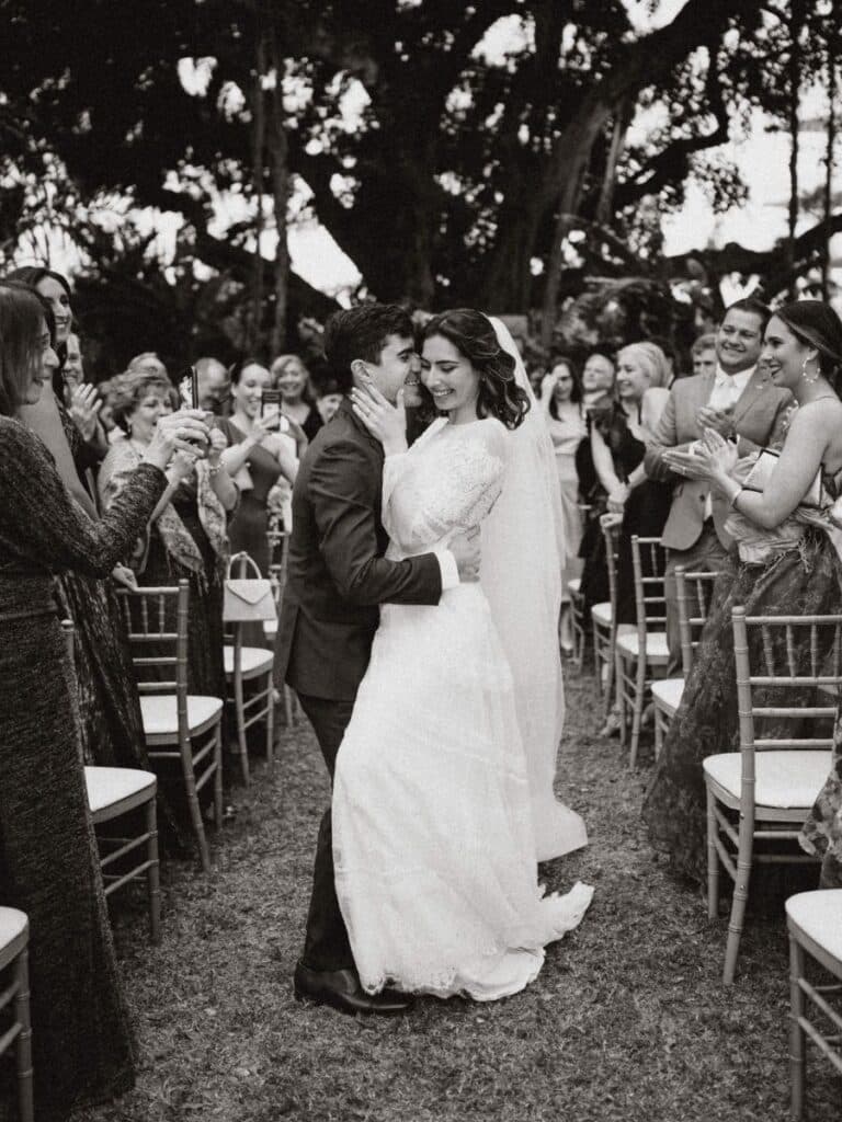 newlyweds sharing a kiss during a garden wedding ceremony in miami beach with guests clapping.