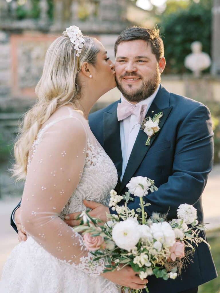 bride and groom sharing a kiss with bride holding a bouquet at vizcaya garden wedding