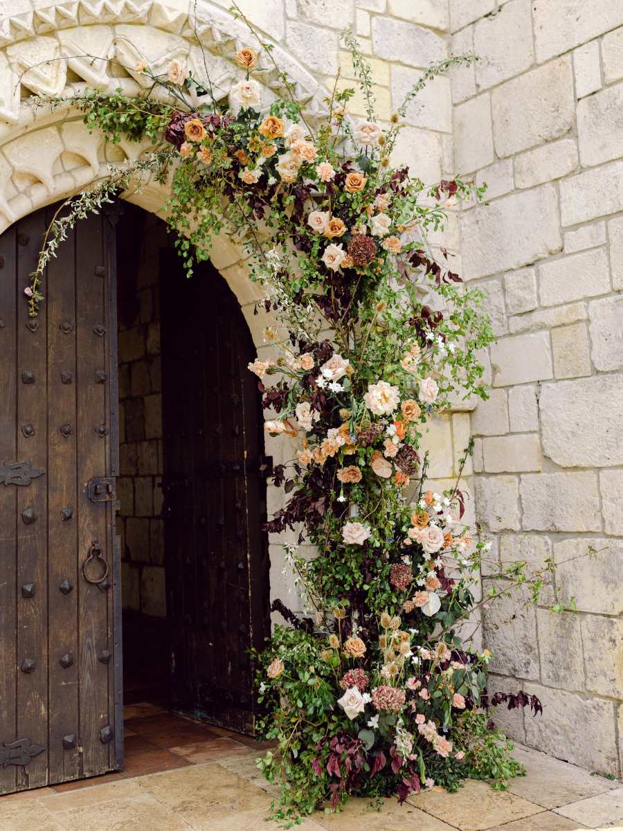 ornate floral arch adorning the entrance to the spanish monastery with a variety of roses and greenery.