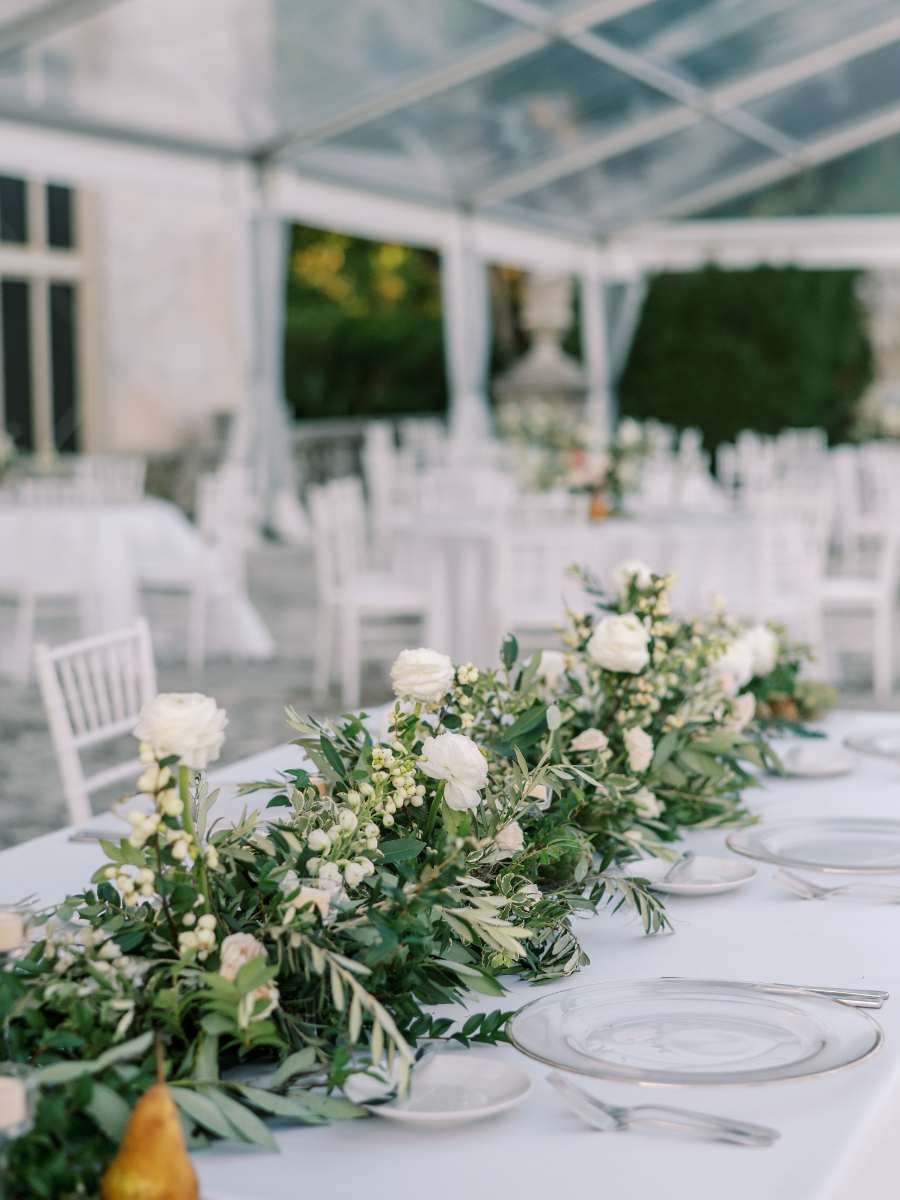 elegant wedding table setting with white floral garland under a clear tent