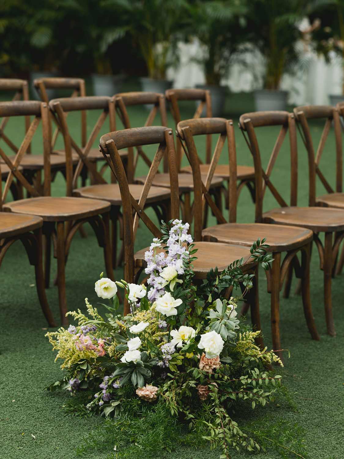 wooden chairs arranged for a wedding ceremony with floral decorations in a garden setting.